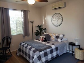 Ein Schlafzimmer mit einem Bett, einem Sessel, einer Topfpflanze, einer Wandklimaanlage und einem Deckenventilator.