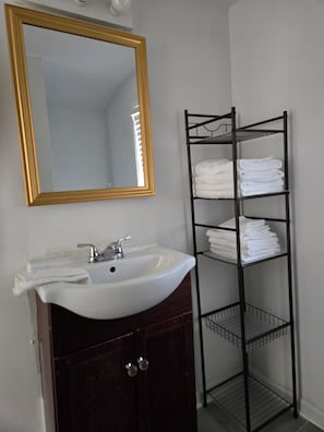 Une salle de bain avec un lavabo blanc, un miroir encadré d’or et un porte-serviettes noir sur lequel sont pliés des serviettes.