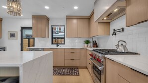 Een moderne keuken met witte aanrechtbladen, houten kastjes, een roestvrijstalen fornuis en een hanglamp.