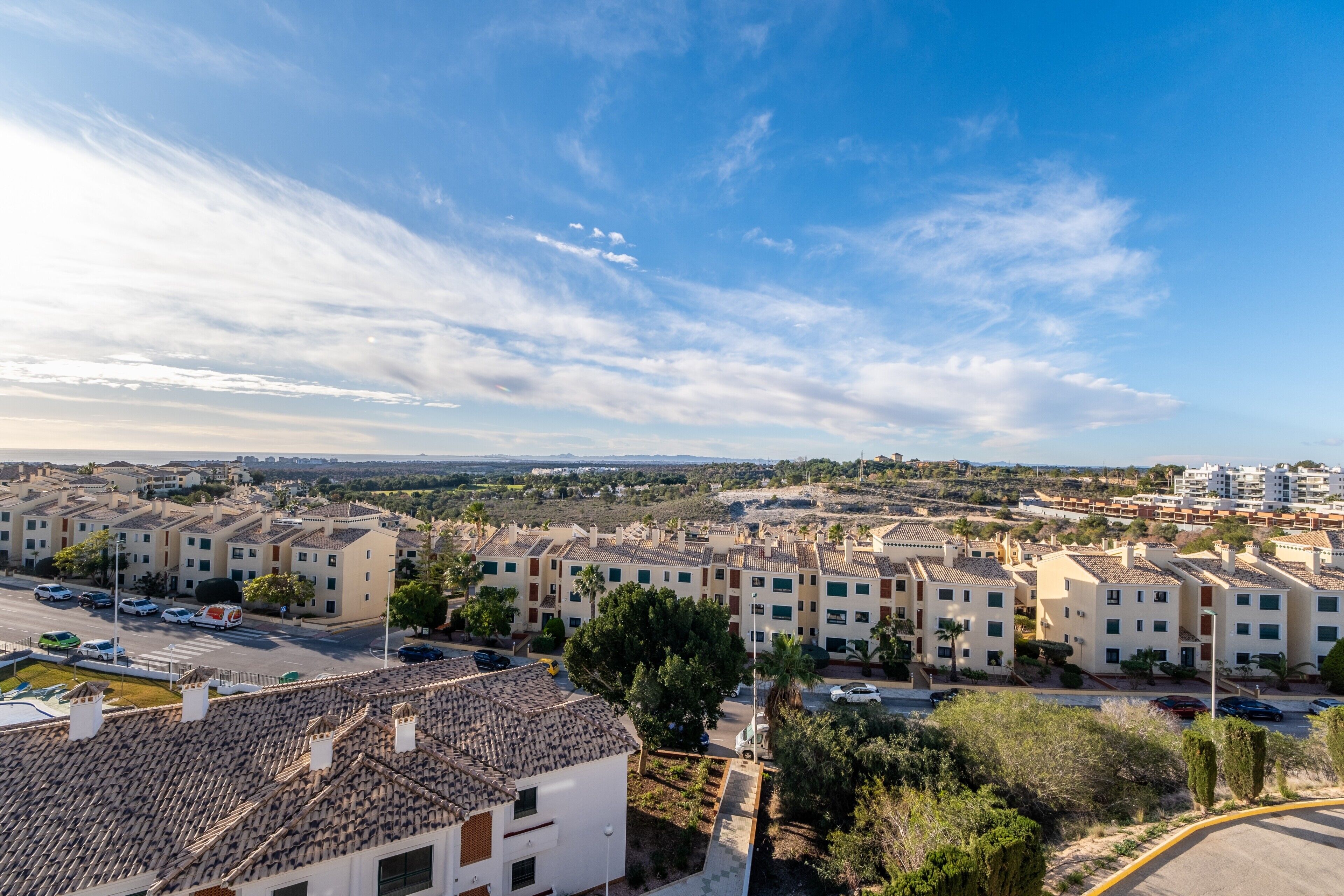 Zona residencial amb edificis de teulades de terracota, cel blau clar i vista llunyana del mar.