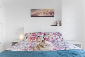 A hotel room with a bed, floral bedspread, a painting above the bed, and a bedside table with a lamp. - Apartment 'Casa Del Alba' with Sea View, Wi-Fi and Air Conditioning (Alicante)