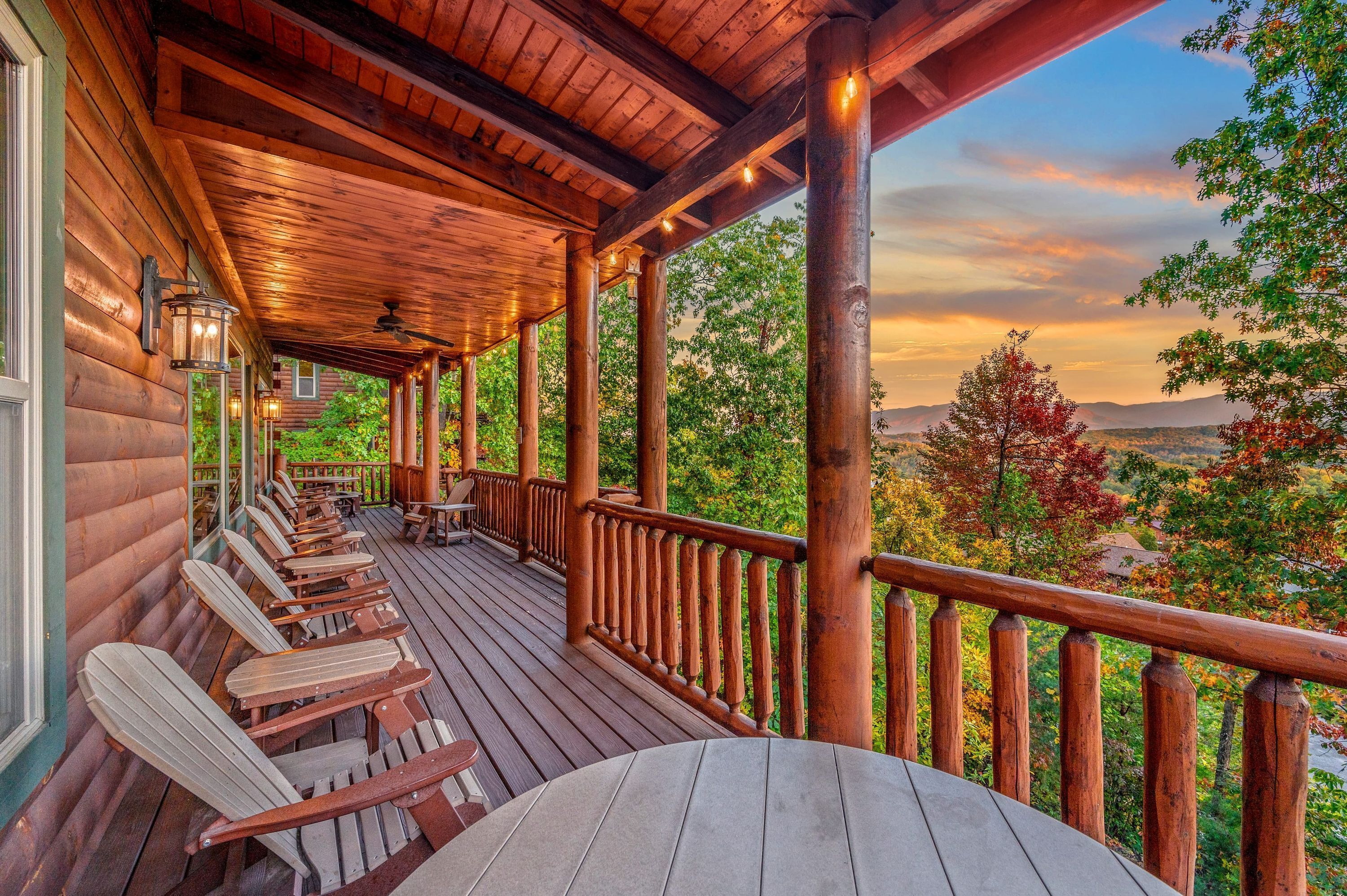 A wooden deck with chairs and a table, overlooking a scenic landscape with trees and mountains.