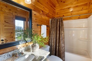 A bathroom with wooden walls, a granite countertop, a white sink, a mirror, a potted plant, a shower curtain, and a white toilet. - A View for All Seasons Luxe Smoky Mountain Cabin With Hot Tubs Game Room (Sevierville)