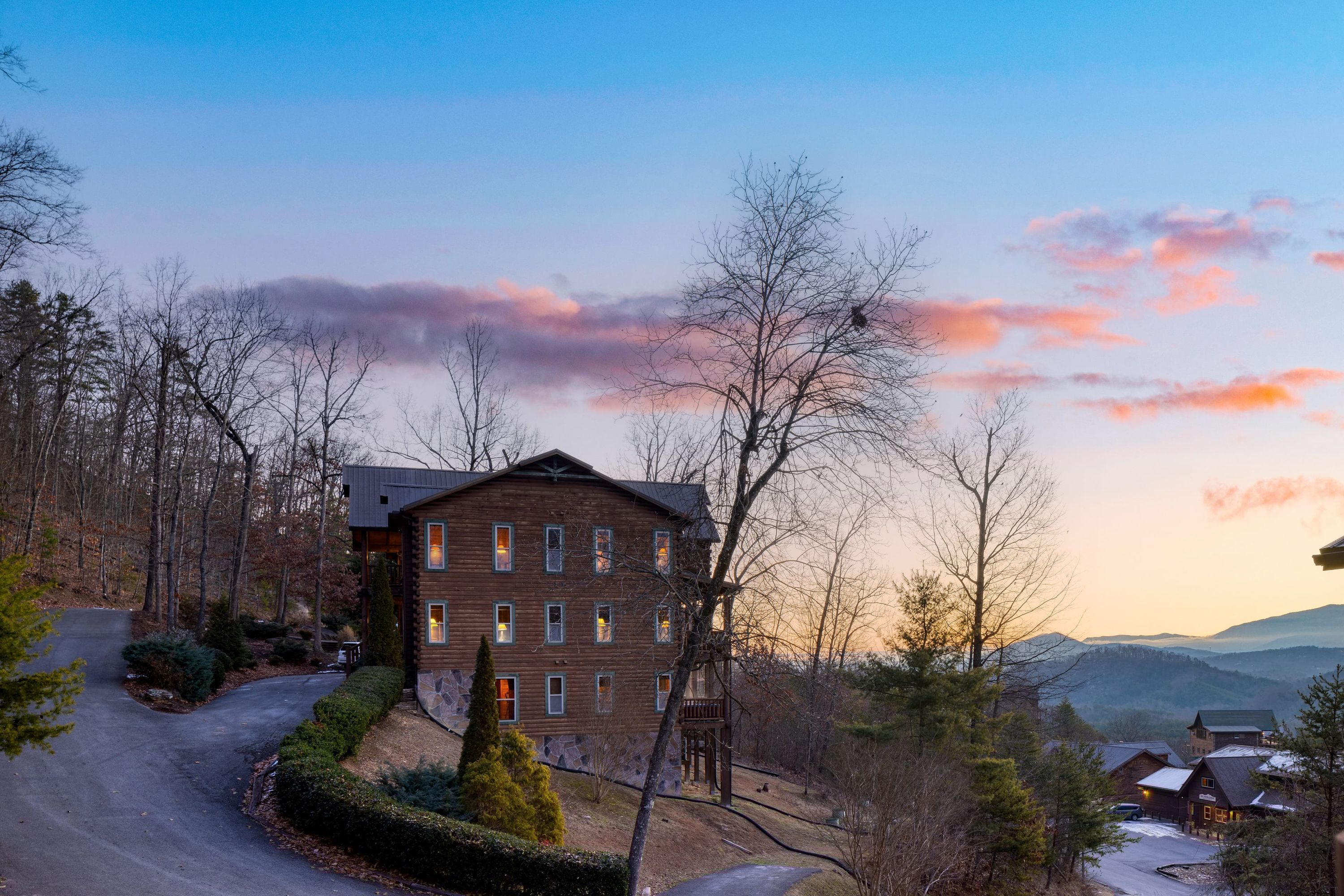 A multi-story lodge with a stone facade, surrounded by trees and a winding driveway.