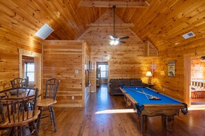 A wooden cabin interior with a pool table, a dining table with chairs, and a ceiling fan. - A View for All Seasons Luxe Smoky Mountain Cabin With Hot Tubs Game Room (Sevierville)