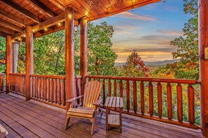 A wooden deck with a wooden chair and table, surrounded by a railing, overlooking a scenic landscape with trees and mountains. - A View for All Seasons Luxe Smoky Mountain Cabin With Hot Tubs Game Room (Sevierville)