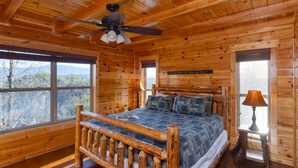A wooden cabin bedroom with a bed, a ceiling fan, and large windows.