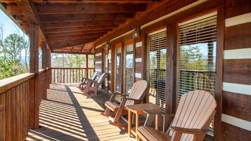 A wooden deck with Adirondack chairs and a covered area with large windows.
