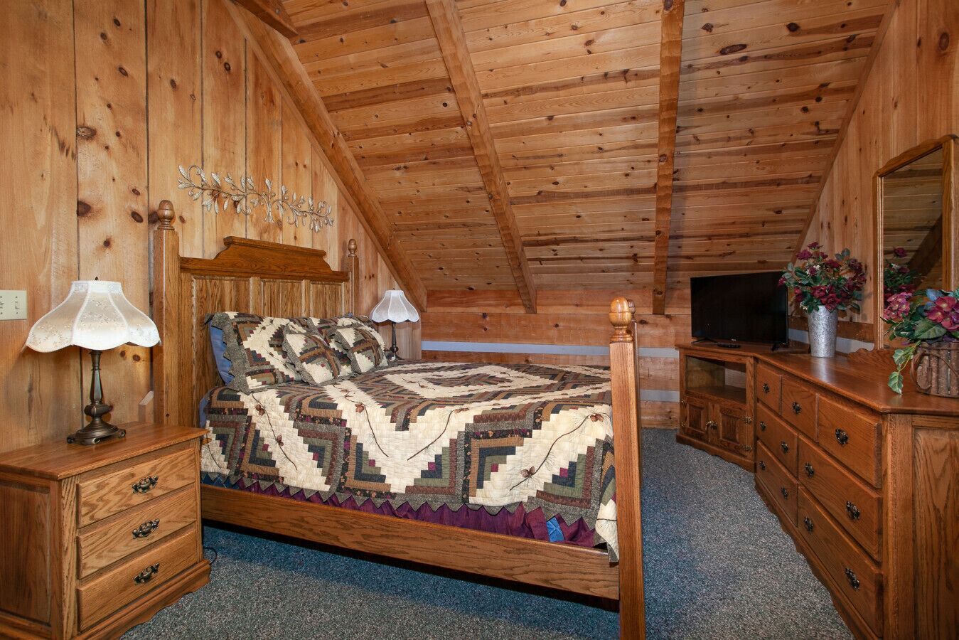 A wooden cabin bedroom with a bed, dresser, and TV.