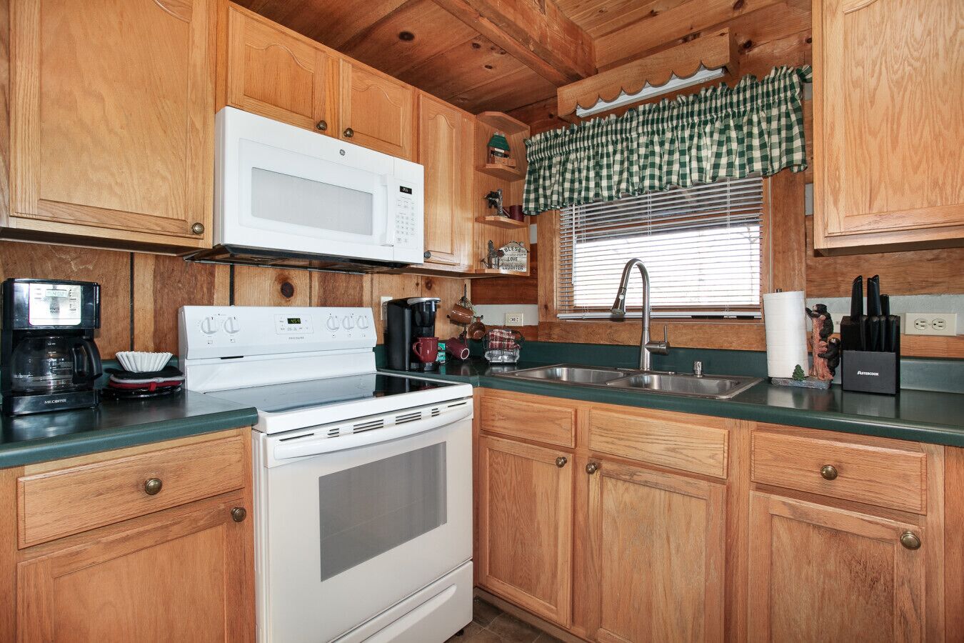 A kitchen with wooden cabinets, a white microwave, a stove, a coffee maker, and a sink.
