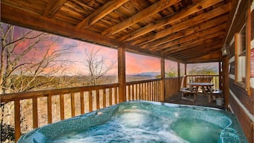 A wooden deck with a hot tub, wooden railing, and a table with chairs.