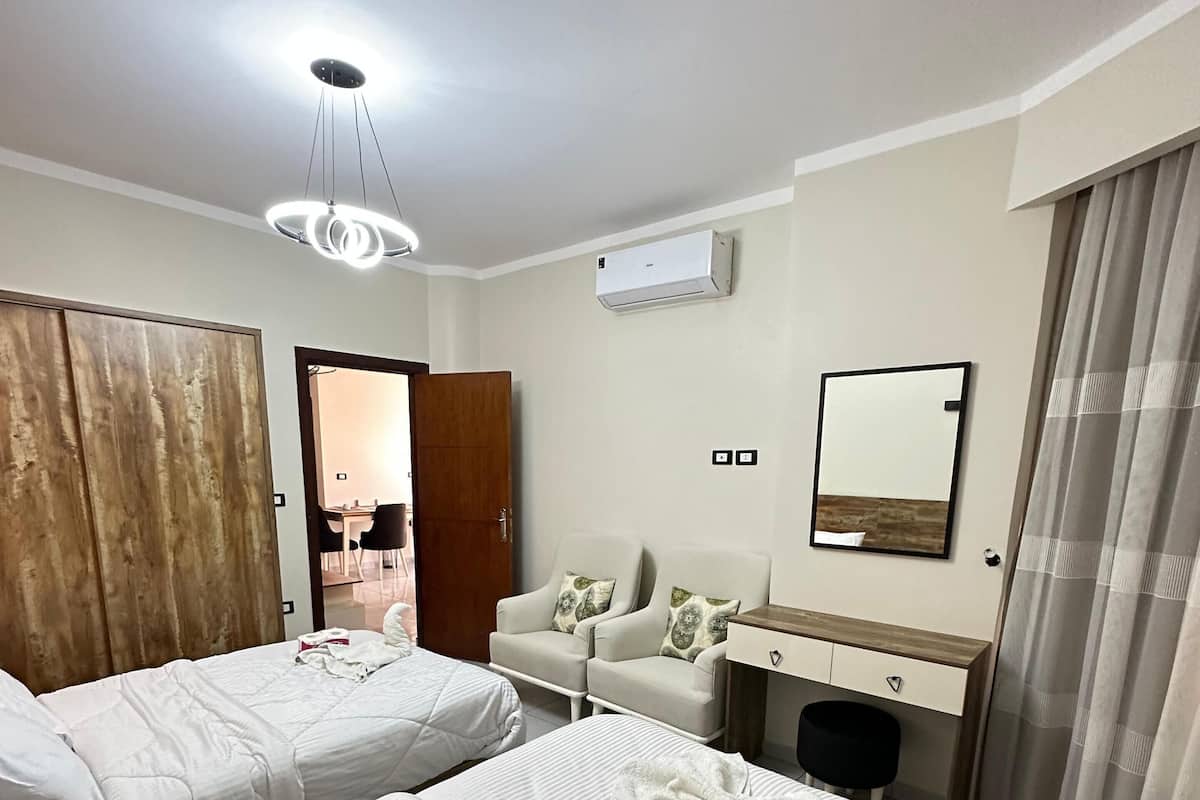 Quarto de hotel com duas camas, uma escrivaninha, uma cadeira, um guarda-roupa e ar condicionado.