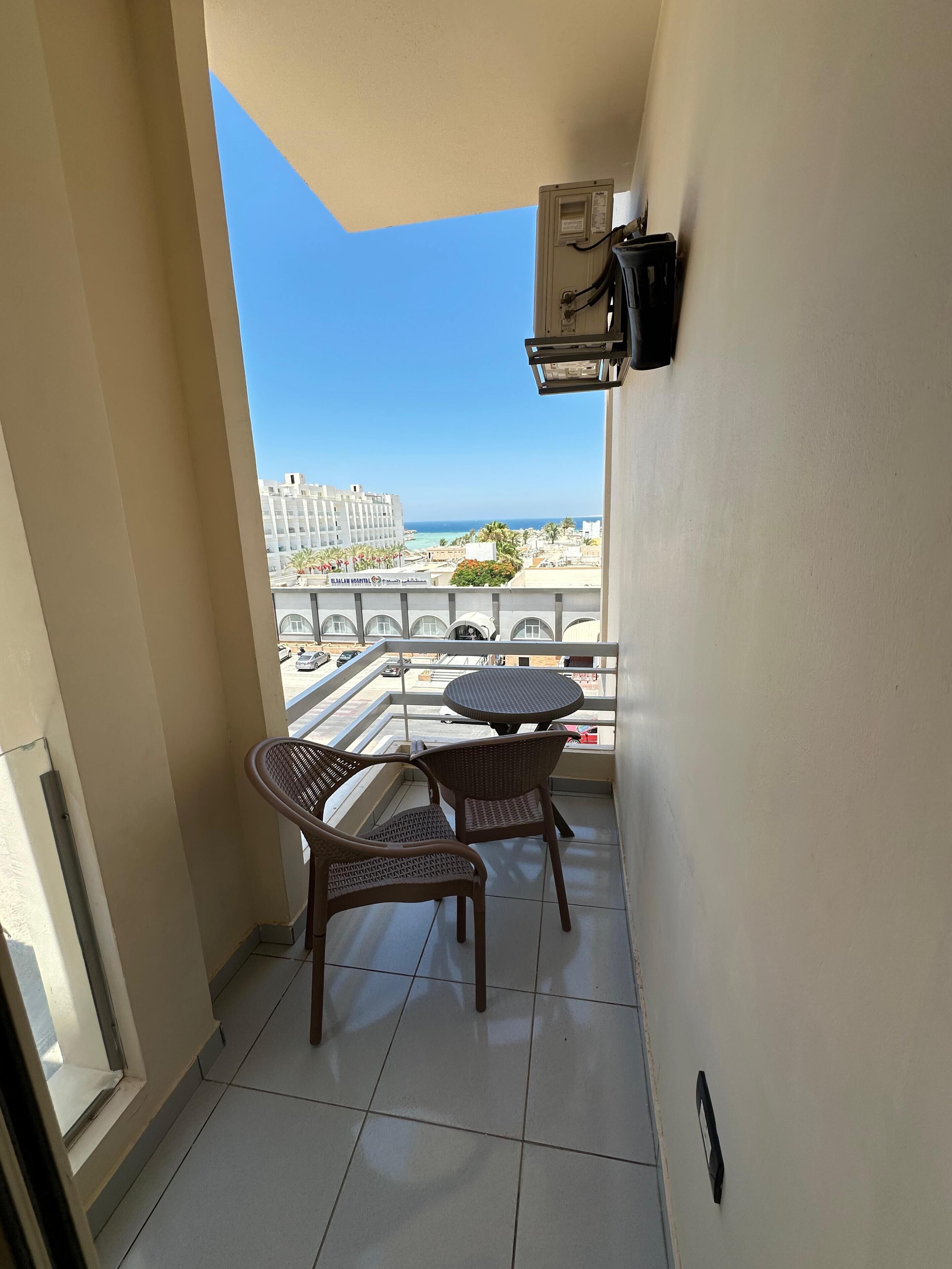 Varanda com duas cadeiras de vime e uma mesa pequena, com vista para um horizonte urbano com edifícios e céu claro.