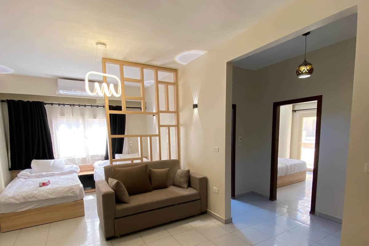 Quarto de hotel moderno com cama, sofá, divisória de madeira e vista para outro quarto.