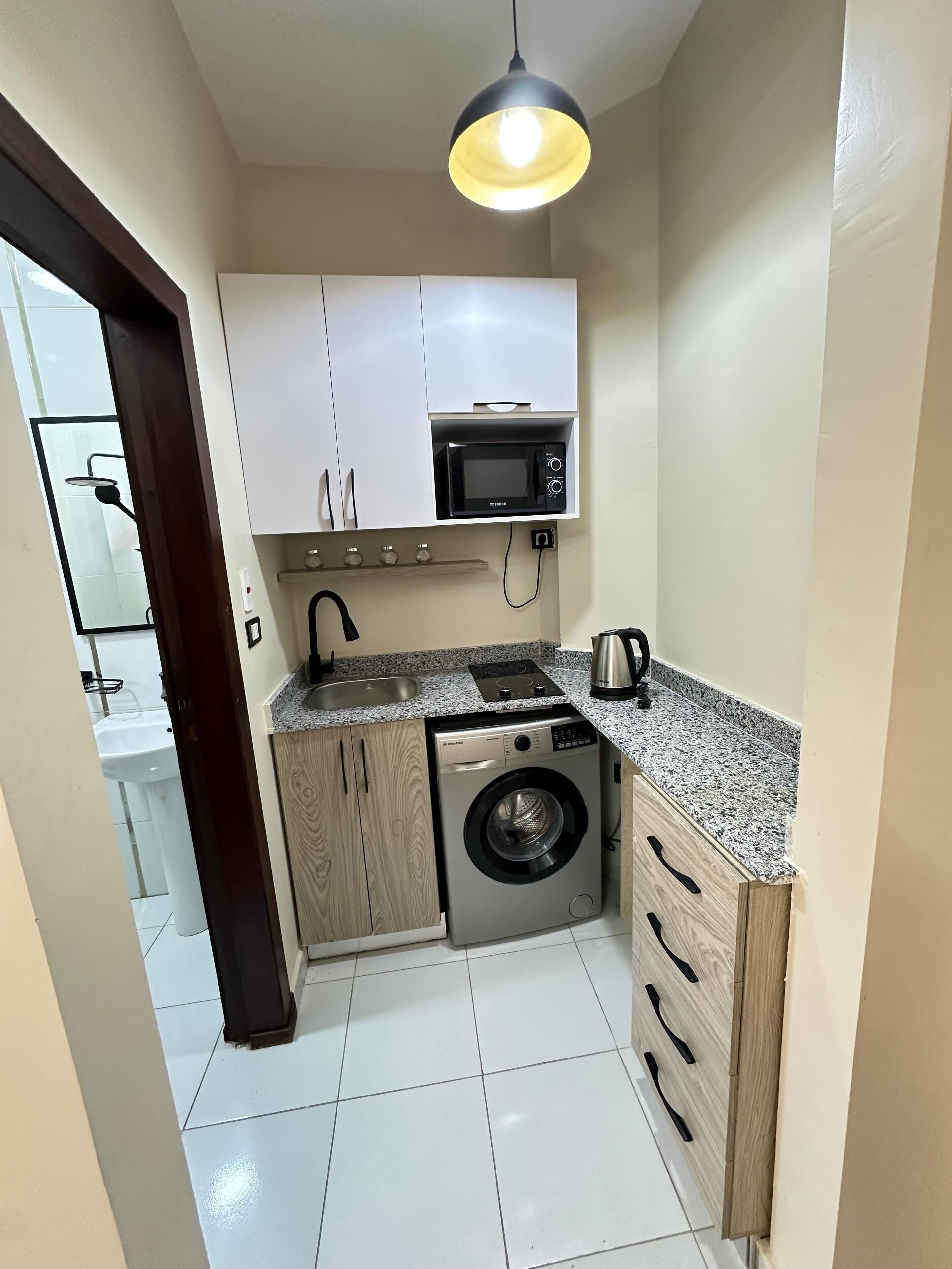 A compact kitchen with a microwave, washing machine, and a sink.