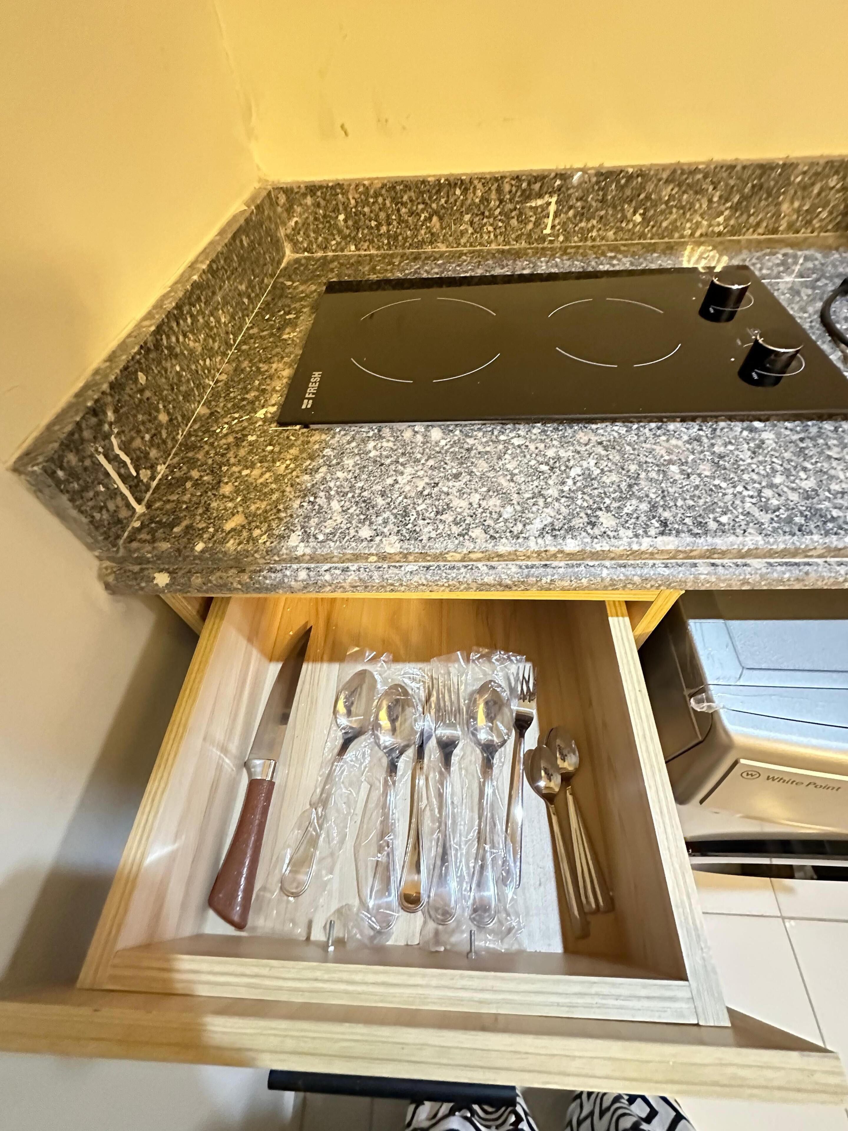 A kitchen with a granite countertop, a built-in stove, and a drawer containing utensils.