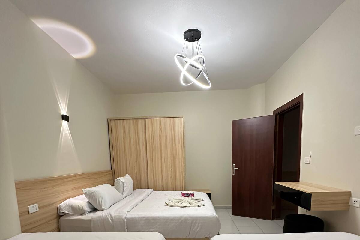 Quarto de hotel com duas camas de solteiro, cabeceira de madeira, televisão de tela plana, guarda-roupa de madeira e luminária no teto.