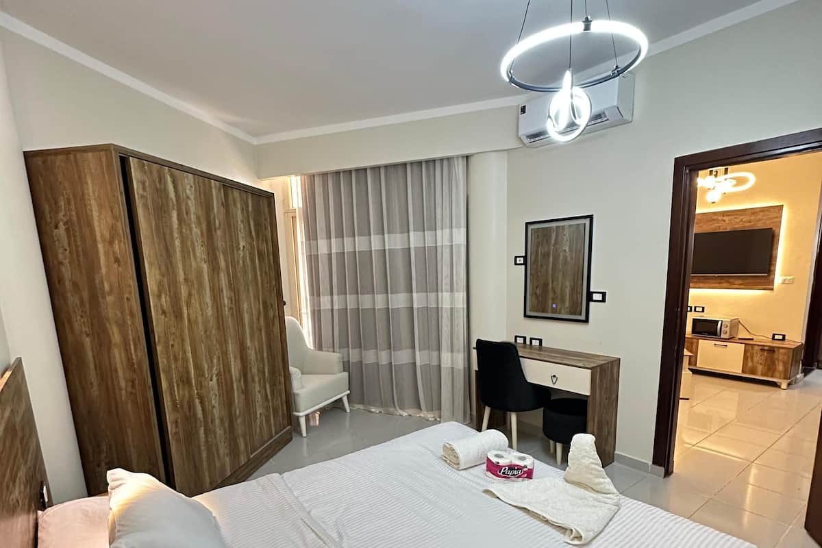Quarto de hotel com uma cama grande, uma escrivaninha, uma cadeira, um guarda-roupa e um banheiro visível por uma porta aberta.