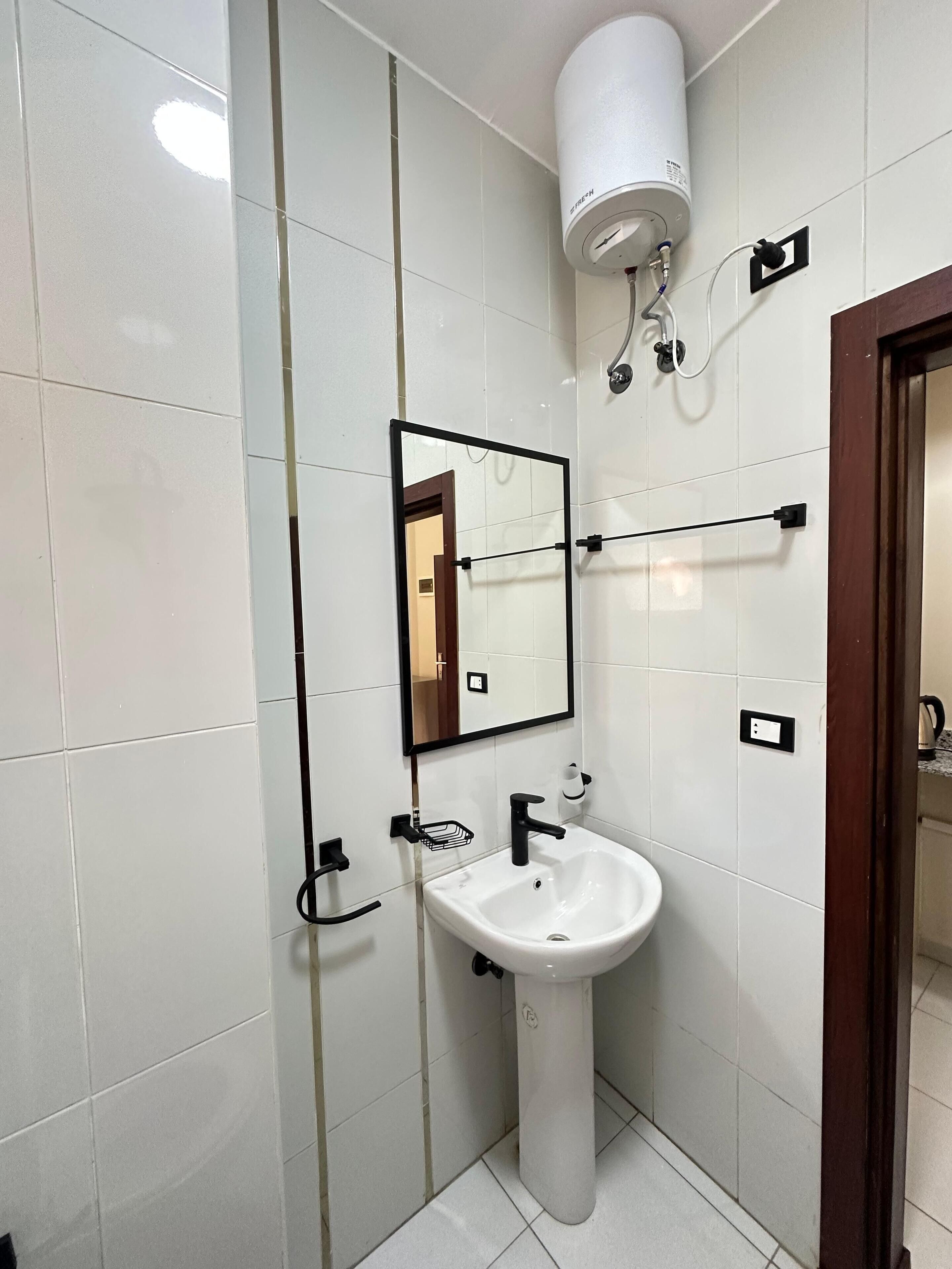 A bathroom with white tiled walls, a white pedestal sink, a mirror, a towel rack, and a hand dryer.