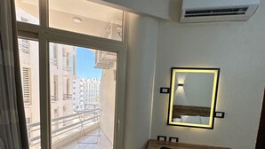 Habitación de hotel con escritorio, silla y un espejo grande con iluminación. Hay una puerta corredera de cristal que da a un balcón exterior.