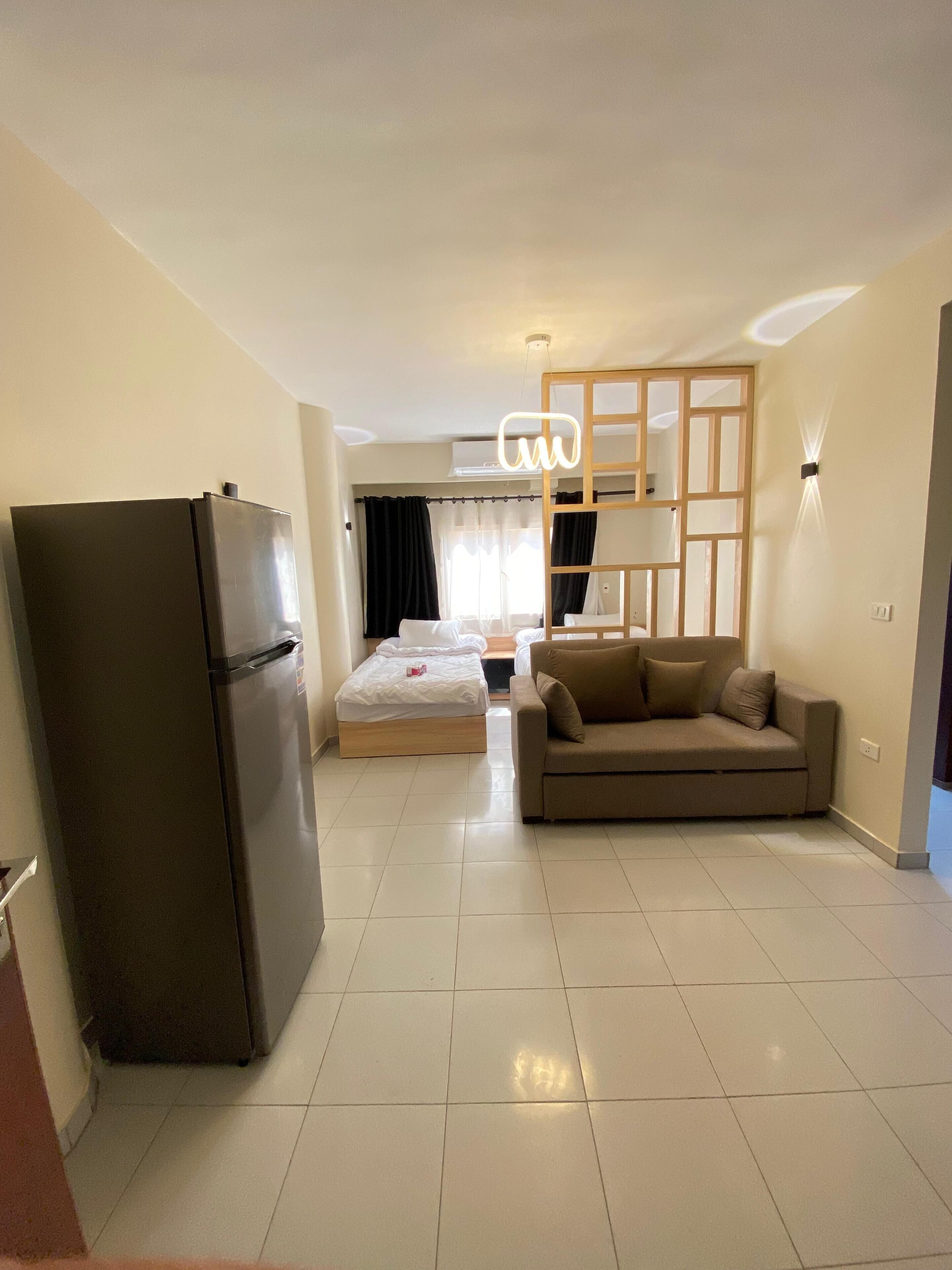 Un espacio habitable compacto con kitchenette, una cama, un sofá y un divisor.