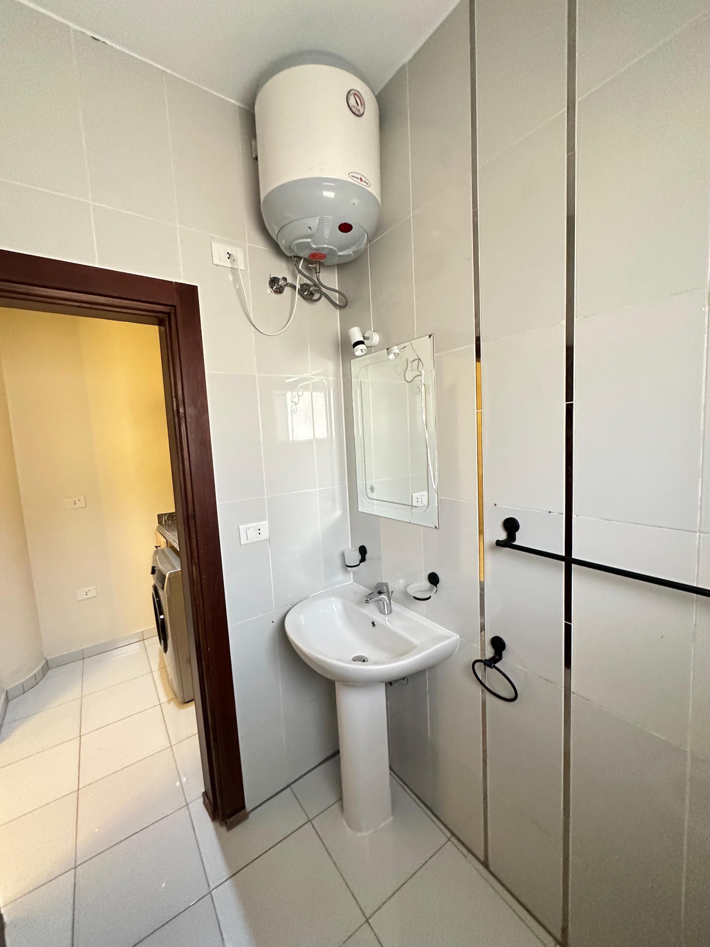 A bathroom with a white sink, a mirror, a towel rack, and a shower with a white wall-mounted heater.