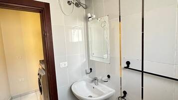 A bathroom with a white sink, a mirror, a towel rack, and a shower with a white wall-mounted heater.
