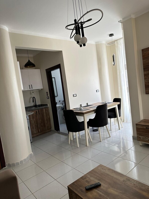 A modern living room with a dining area, a kitchen in the background, and a wooden table with a remote control. - Downtown Keys (Hurghada)
