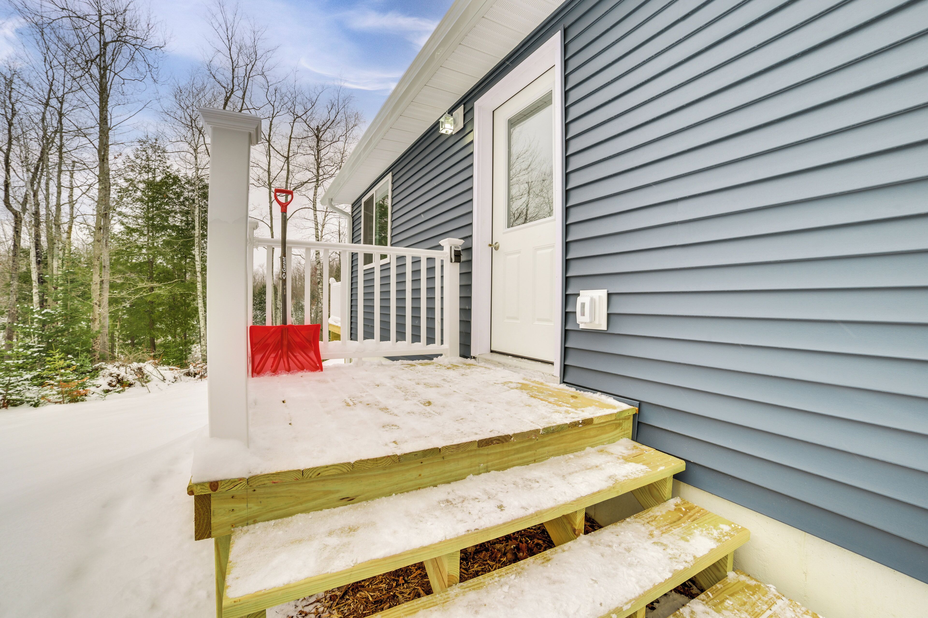 A wooden deck with steps leading to a white door, surrounded by snow and trees.