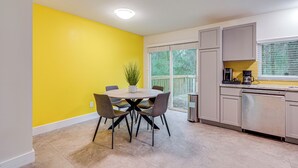 A modern kitchen with a yellow accent wall, a dining area with a round table and chairs, and a view of the outdoors through a large window. - Family Retreat w/ Pool Table Near the Woodlands! (Spring)