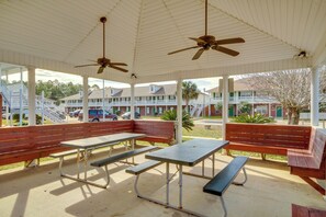 Relax in a serene outdoor space with picnic tables and benches, sheltered by a roof and ceiling fans.