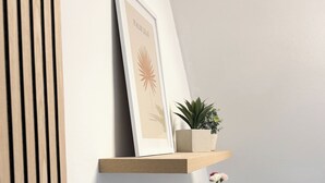 Una estantería de madera con un cuadro enmarcado, una pequeña planta en maceta y un florero con flores.