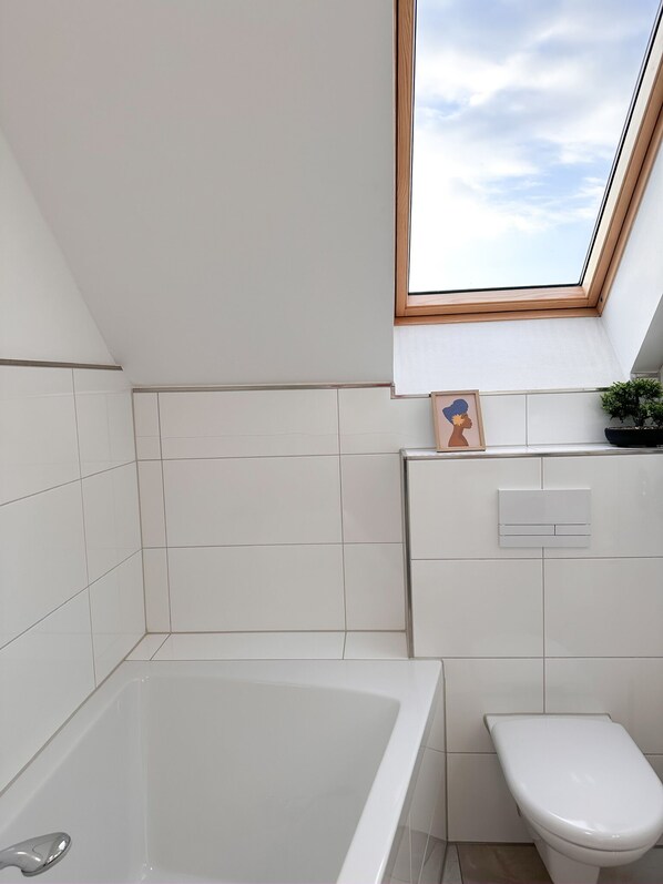 Une salle de bain moderne avec un puits de lumière, des carreaux blancs, une baignoire et des toilettes.