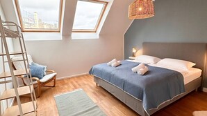 Un dormitorio con techo estilo loft, dos tragaluces, una cama con ropa de cama azul, una escalera de madera y una lámpara de fibra natural.