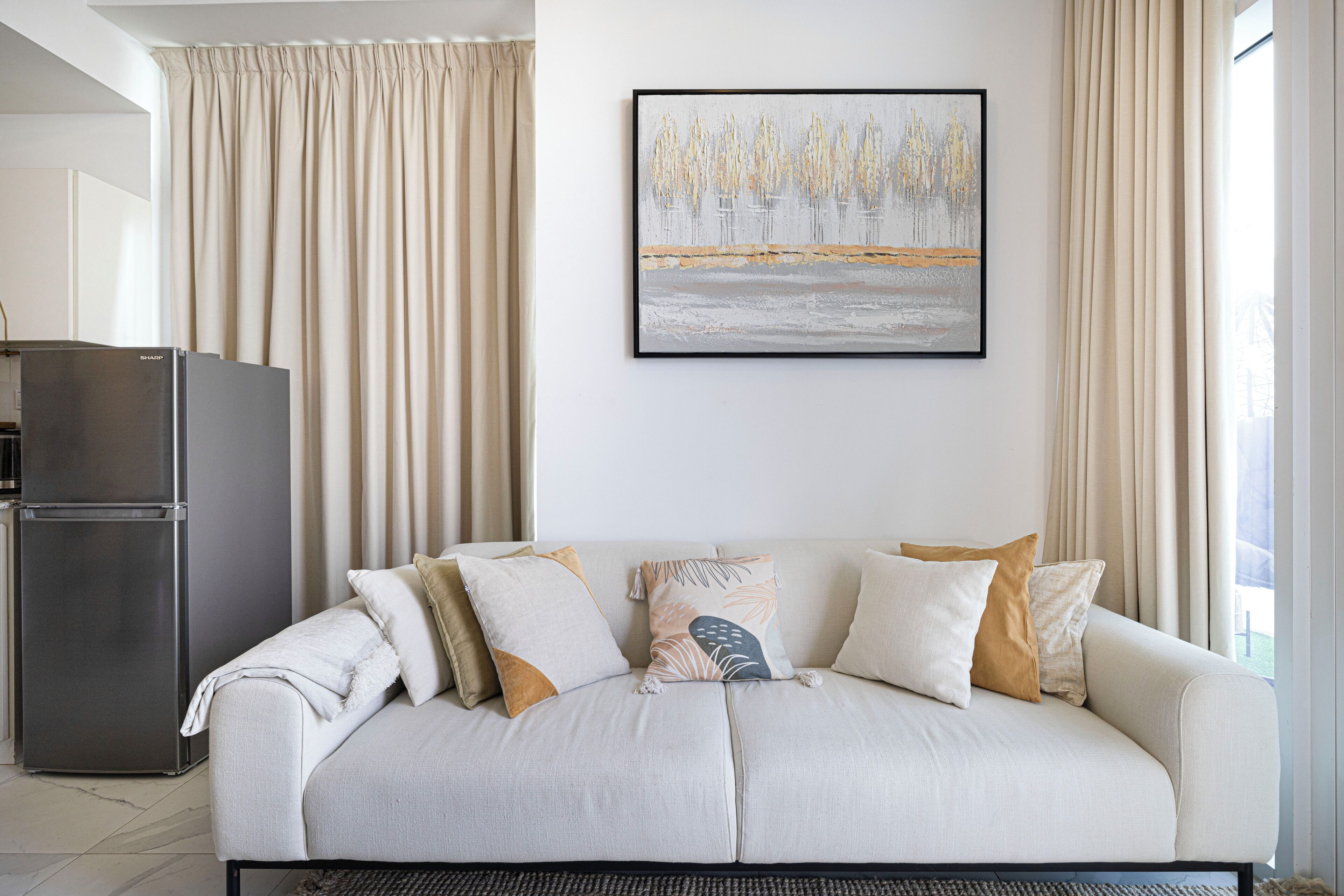 A modern living room with a sofa, a framed artwork, and a refrigerator.