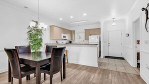 A modern kitchen with wooden cabinets, a central island, and a dining area with a glass table and chairs. - Myrtlewood 2-bedroom condo.  Pool in the backyard (Myrtle Beach)