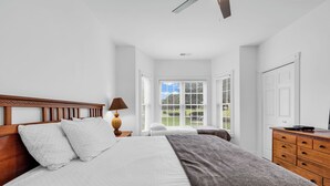 A bedroom with a wooden headboard, a bed with white and gray bedding, a nightstand with a lamp, and a dresser with drawers. - Myrtlewood 2-bedroom condo.  Pool in the backyard (Myrtle Beach)