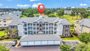 A multi-story hotel with a central courtyard, parking, and a golf course in the background. - Myrtlewood 2-bedroom condo.  Pool in the backyard (Myrtle Beach)