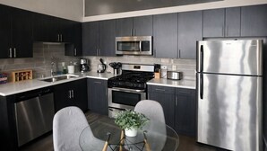 Una cocina moderna con gabinetes oscuros, electrodomésticos de acero inoxidable, una mesa de comedor de vidrio y una planta en maceta.