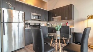 Una cocina moderna con armarios oscuros, electrodomésticos de acero inoxidable y una mesa redonda de vidrio con sillas negras.