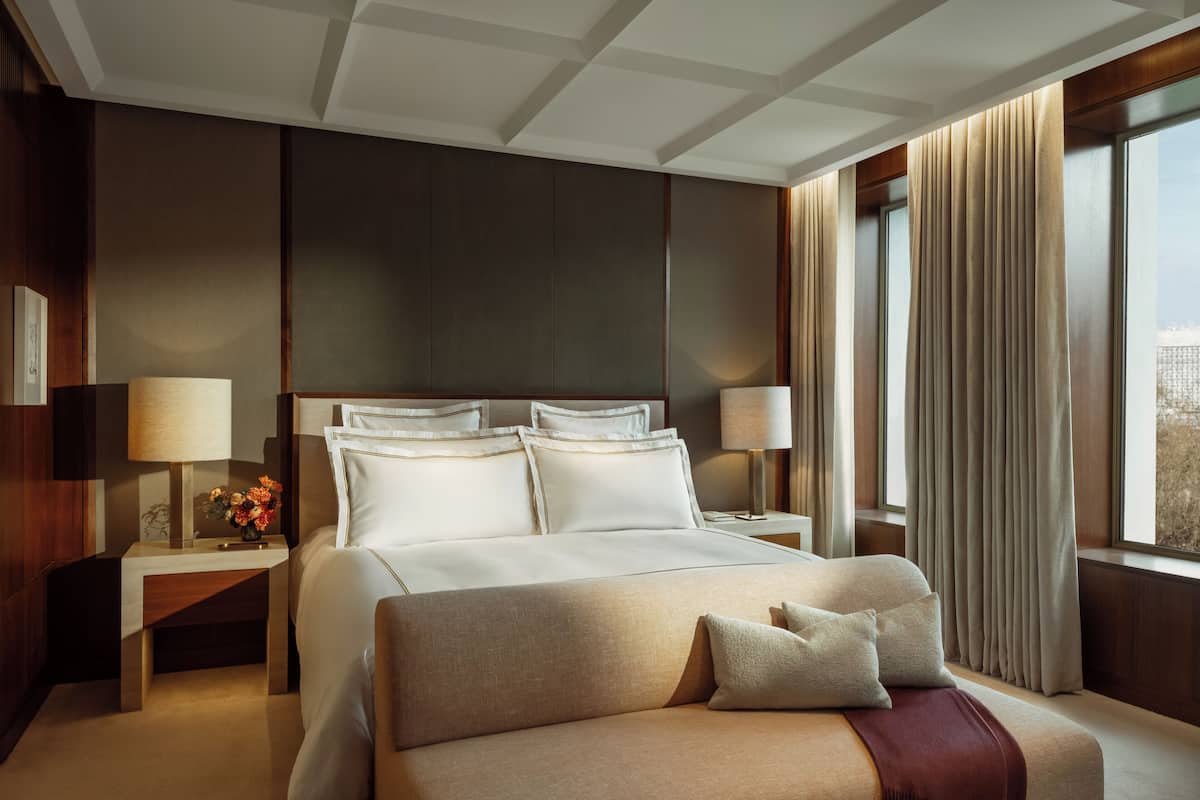 A hotel room with a large bed, two bedside tables, a nightstand, a lamp, and a window with curtains.