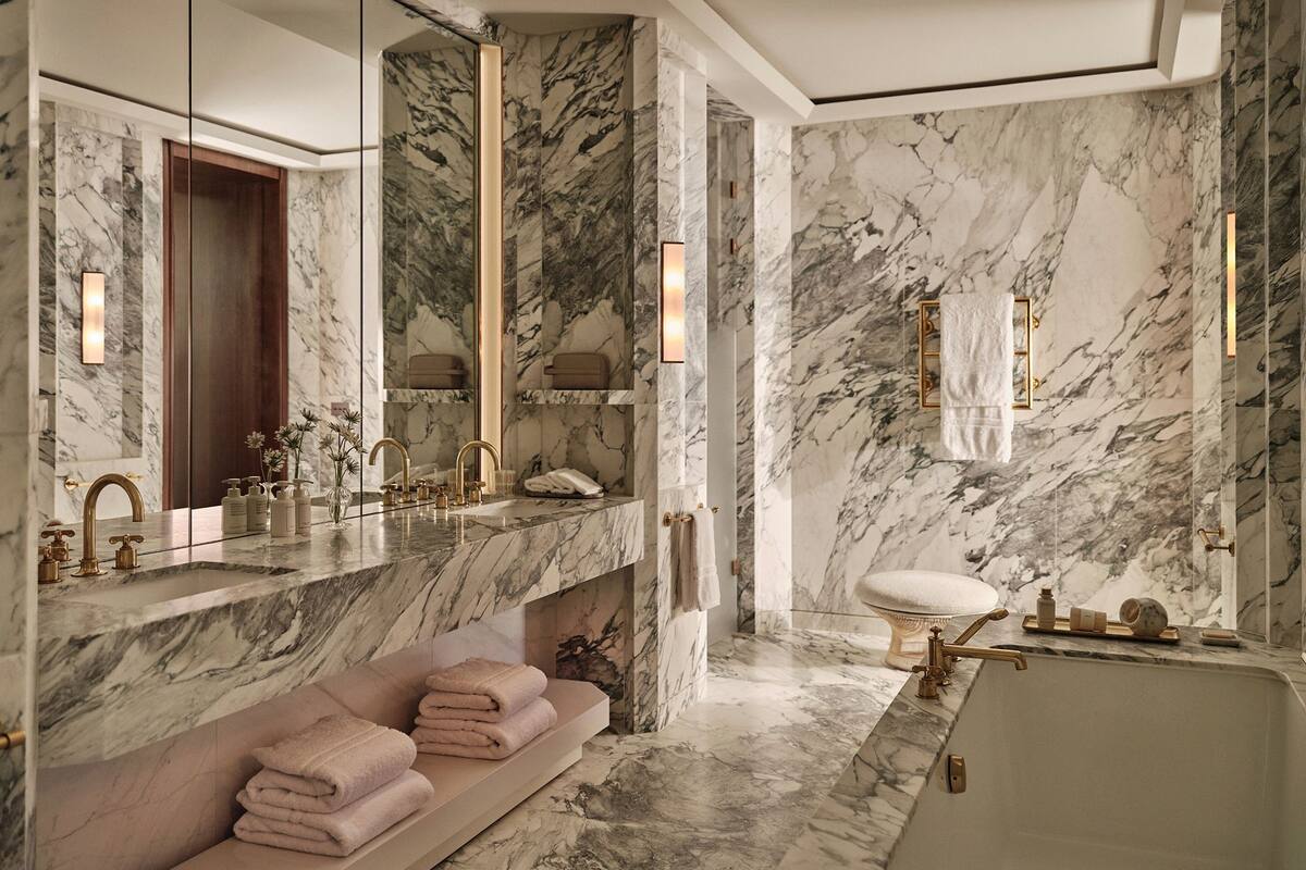 A luxurious bathroom with marble walls, a large mirror, a double sink, and a bathtub.