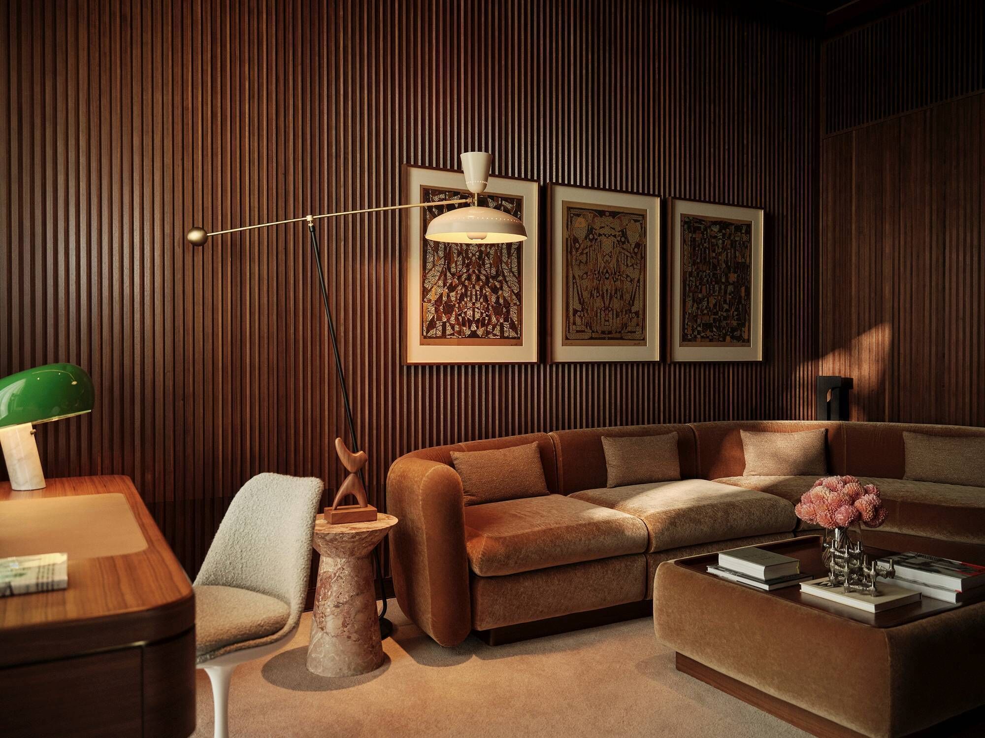A modern living room with a brown leather sofa, a green desk lamp, a floor lamp, and framed artwork on the wall.