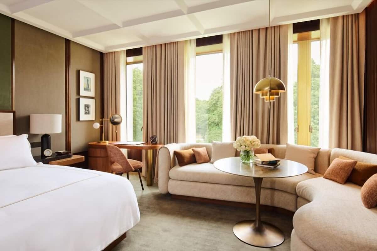 A hotel room with a bed, a sofa, a small table, a desk, and a window with curtains.