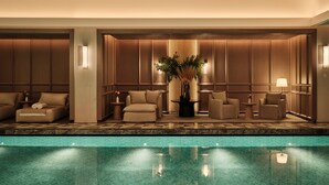 Vestíbulo de hotel con piscina, que presenta zonas de estar con sofás y sillones, una planta central y suelo de mármol.