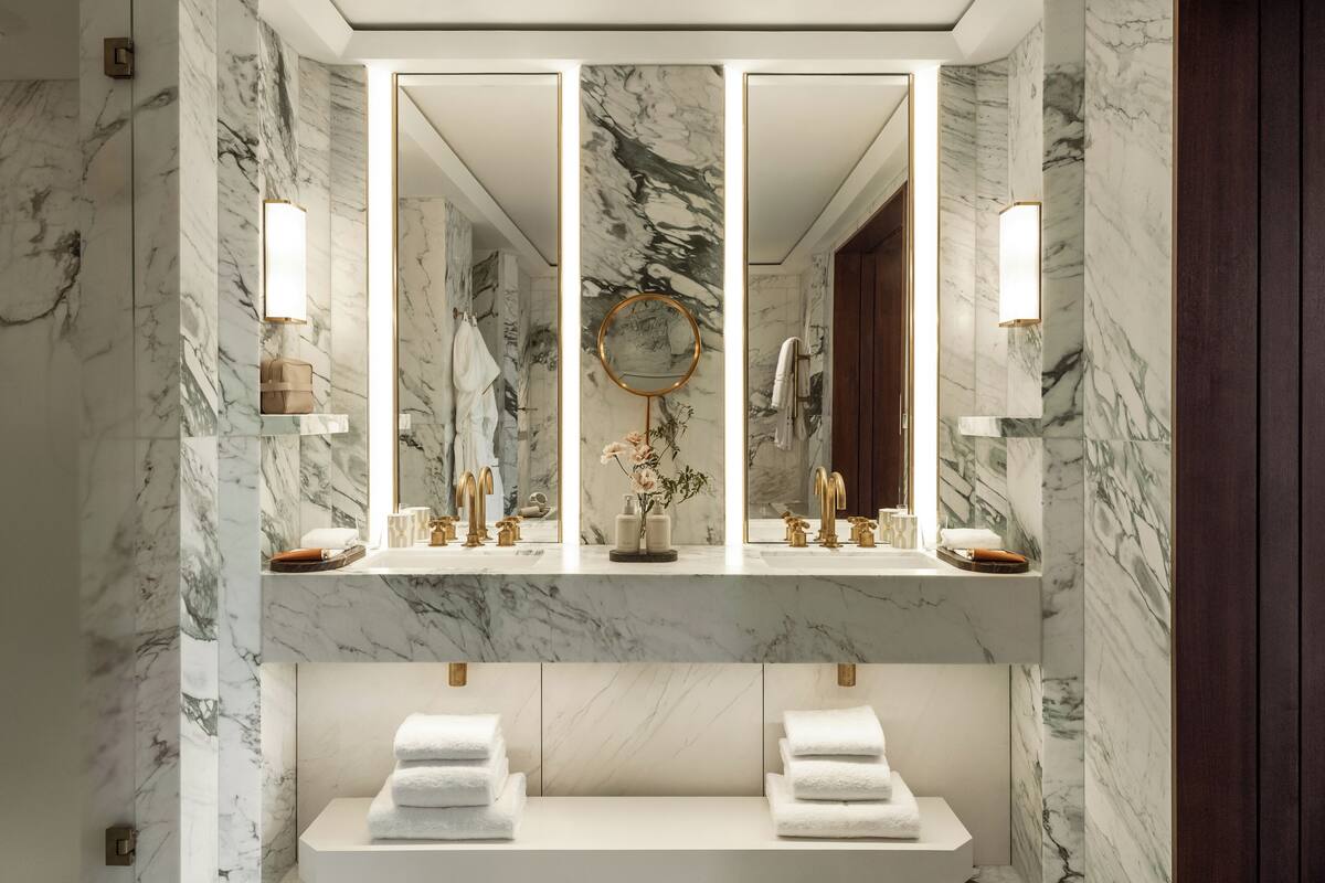 A bathroom with marble walls, a large mirror, and two sinks with towel racks.