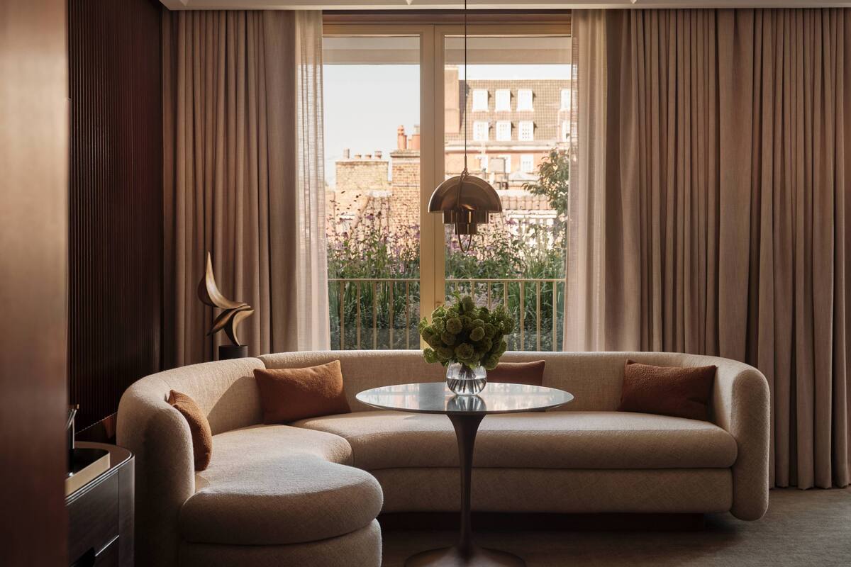 A modern living room with a beige sofa, a round glass coffee table, and a view of a cityscape through large windows.