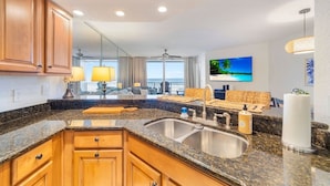 A kitchen with granite countertops, wooden cabinets, a double sink, and a dining area with a view of the ocean.