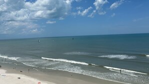 A beach with waves, a clear sky, and a few boats.