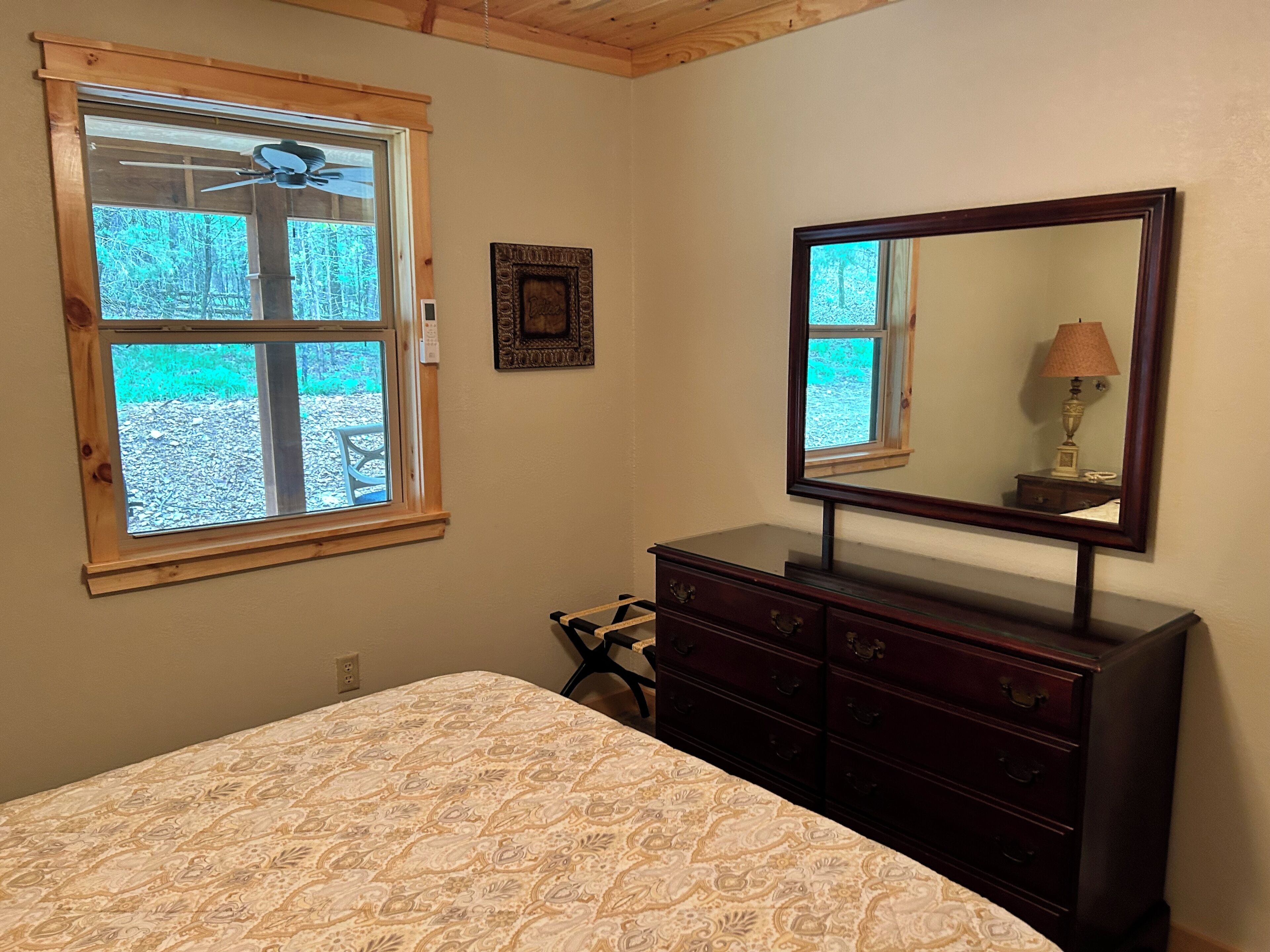 Un dormitorio con cama, cómoda, espejo y ventana con ventilador de techo.
